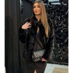 Crna duža bunda od prirodnog nerca sa kapom, dugmetom i pojasom, uz mogućnost skraćivanja, pruža luksuz i savršeno pristajanje.